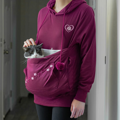 A person wearing a maroon hoodie with a cat in the front pocket.