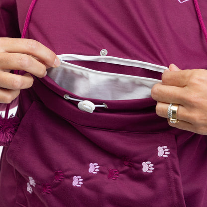 Close-up of a person's hands demonstrating the interior pocket and drawstring closure of a burgundy athletic hoodie with small pink paw print embroidery.