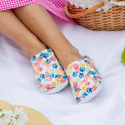 Colorful floral clogs on feet, resting on a picnic blanket with fruits.