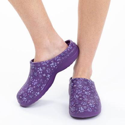 Purple clogs with paw print pattern worn by a person on a white background