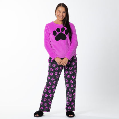 A woman wearing a soft magenta long-sleeve shirt with a black paw print design on the center and a pair of soft black pants patterned with white polka dots and magenta paw prints.