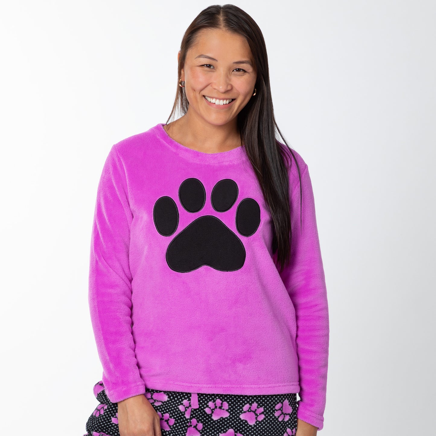 A woman wearing a soft magenta long-sleeve shirt with a black paw print design on the center and a pair of soft black pants patterned with white polka dots and magenta paw prints.