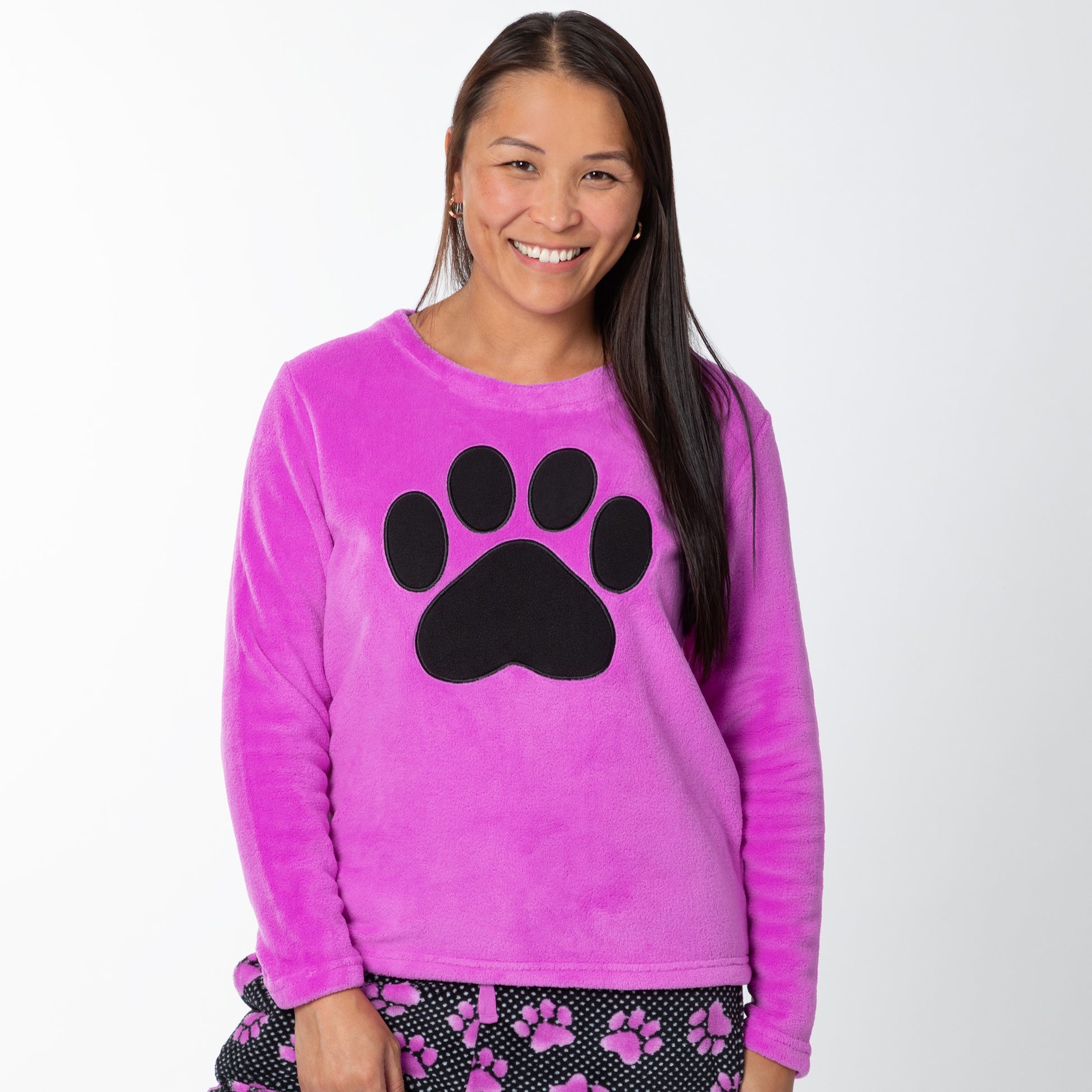 A woman wearing a soft magenta long-sleeve shirt with a black paw print design on the center and a pair of soft black pants patterned with white polka dots and magenta paw prints.