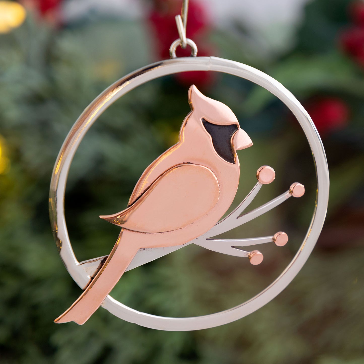 Copper cardinal bird ornament on a branch with a silver circular frame against a blurred green background.