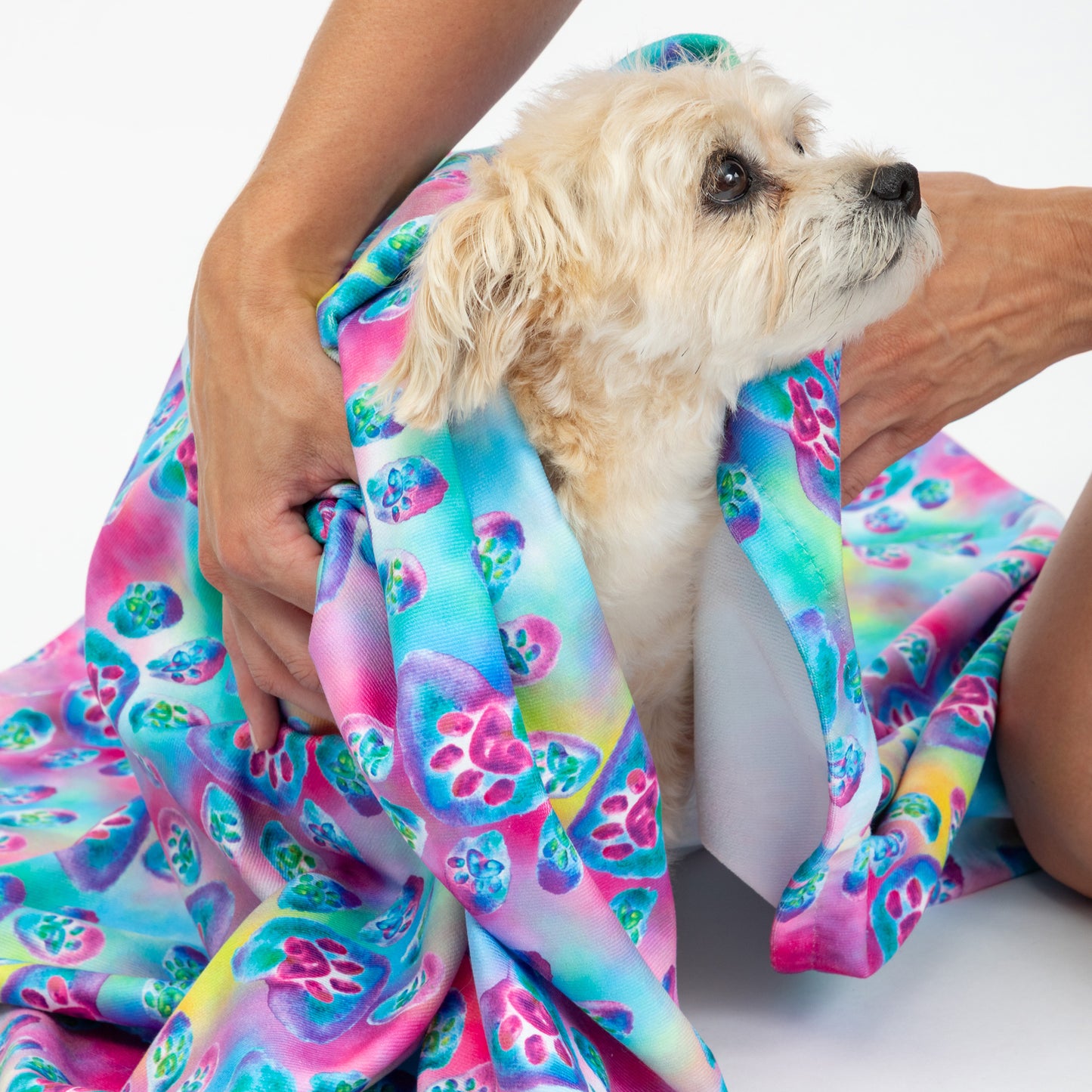 A small dog wrapped in a tie-dye beach towel