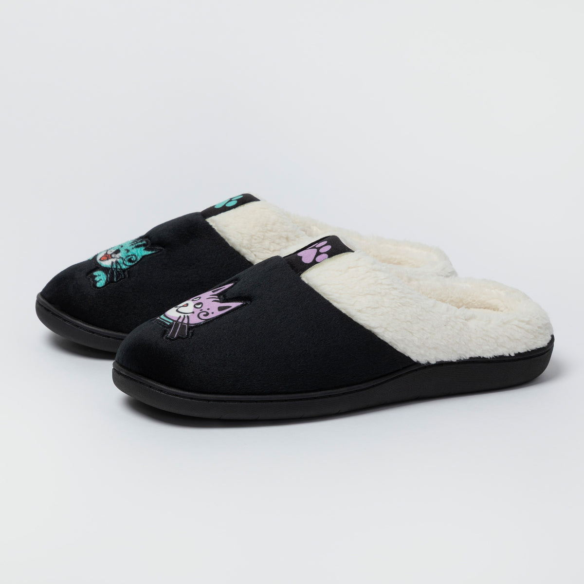 A pair of black slip-on slippers with a soft white fleece lining and embroidered cat faces on the top, shown on a light gray studio background.