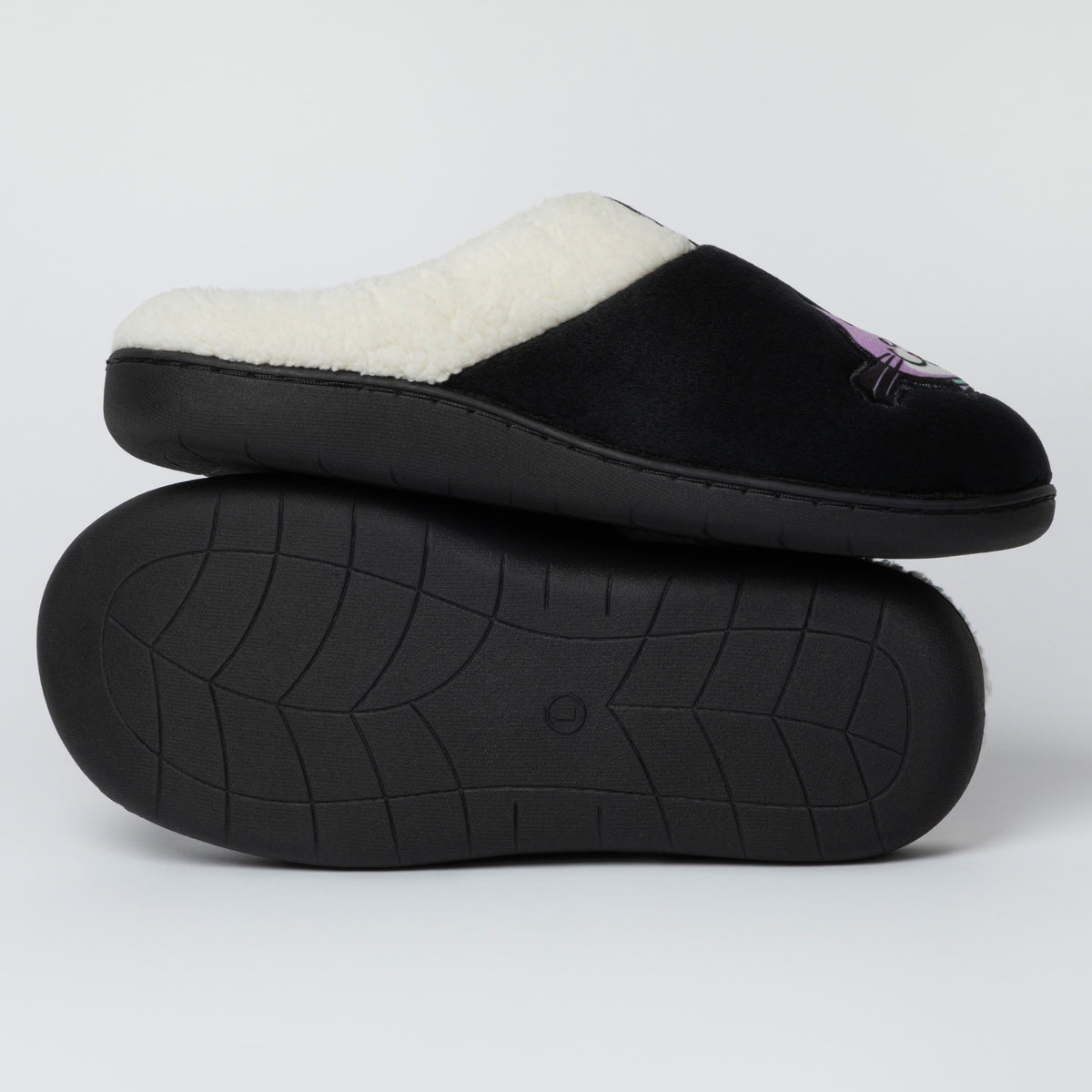 A pair of black slip-on slippers with a white sherpa lining, with one slipper stacked on top of the other to show the textured black sole.