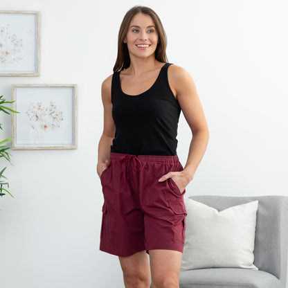 Woman wearing a black tank top and maroon shorts standing in a living room.