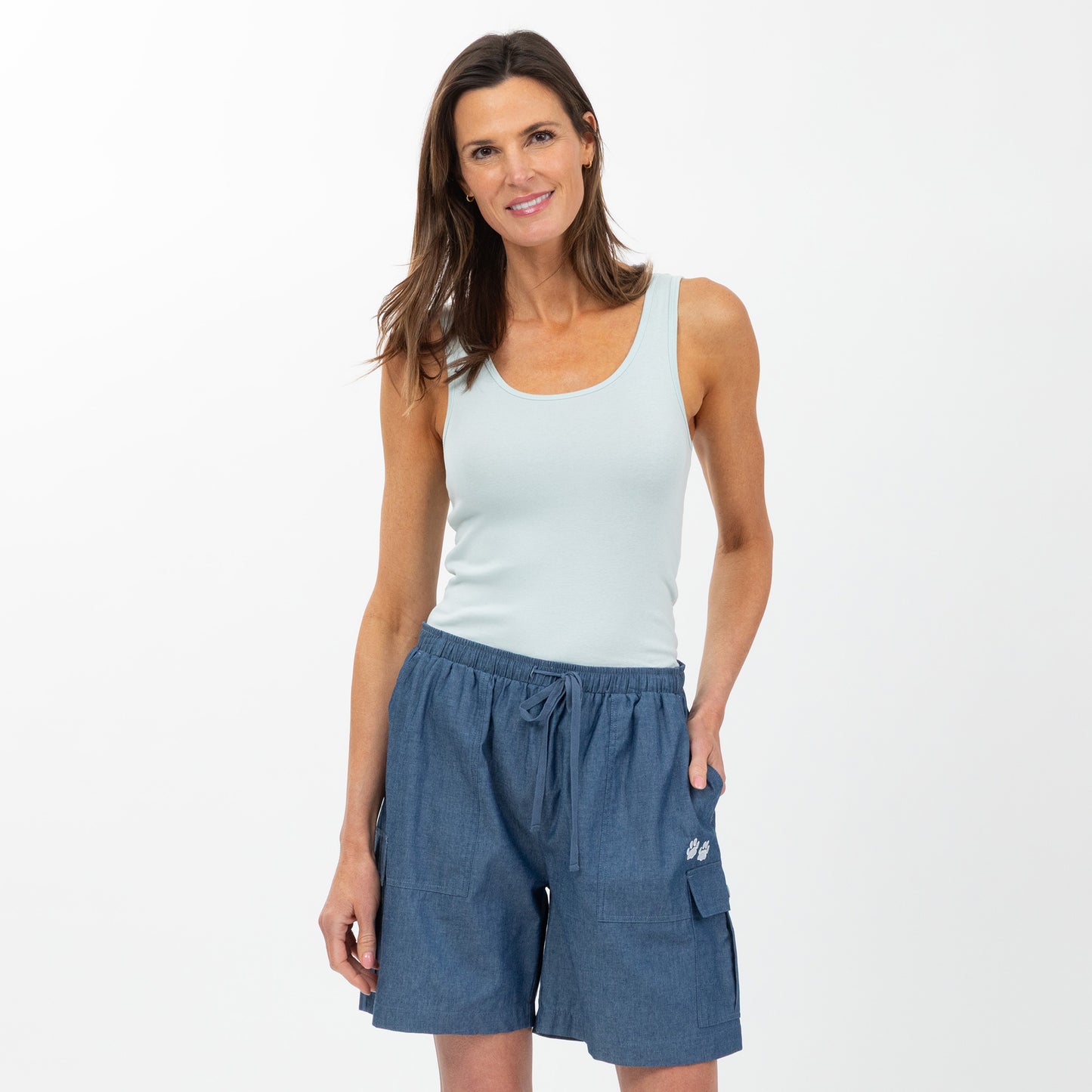 Woman wearing a light blue tank top and chambray cargo shorts on a white background