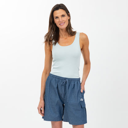 Woman wearing a light blue tank top and chambray cargo shorts on a white background