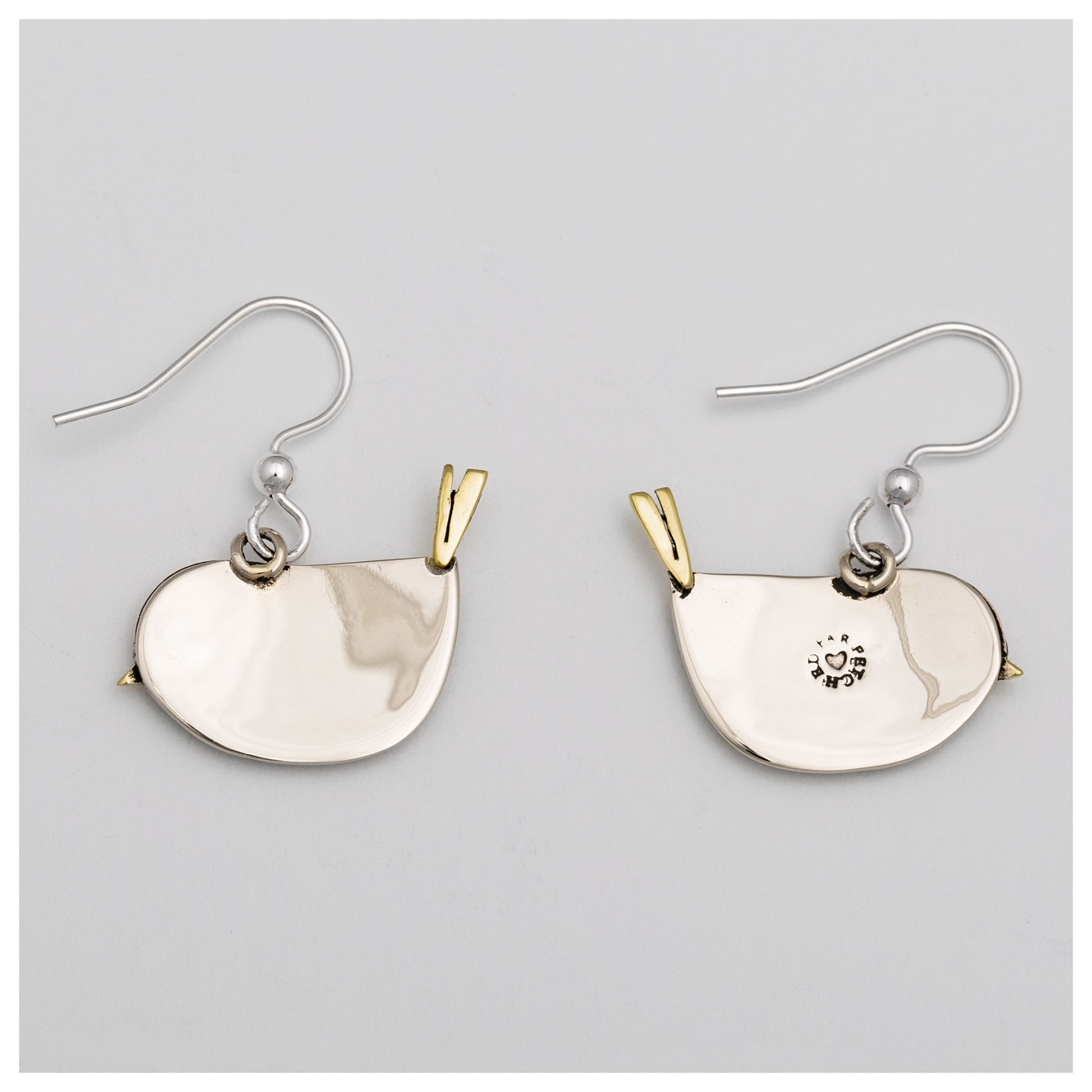The silver and brass backs of bird shaped earrings, against a light gray background.