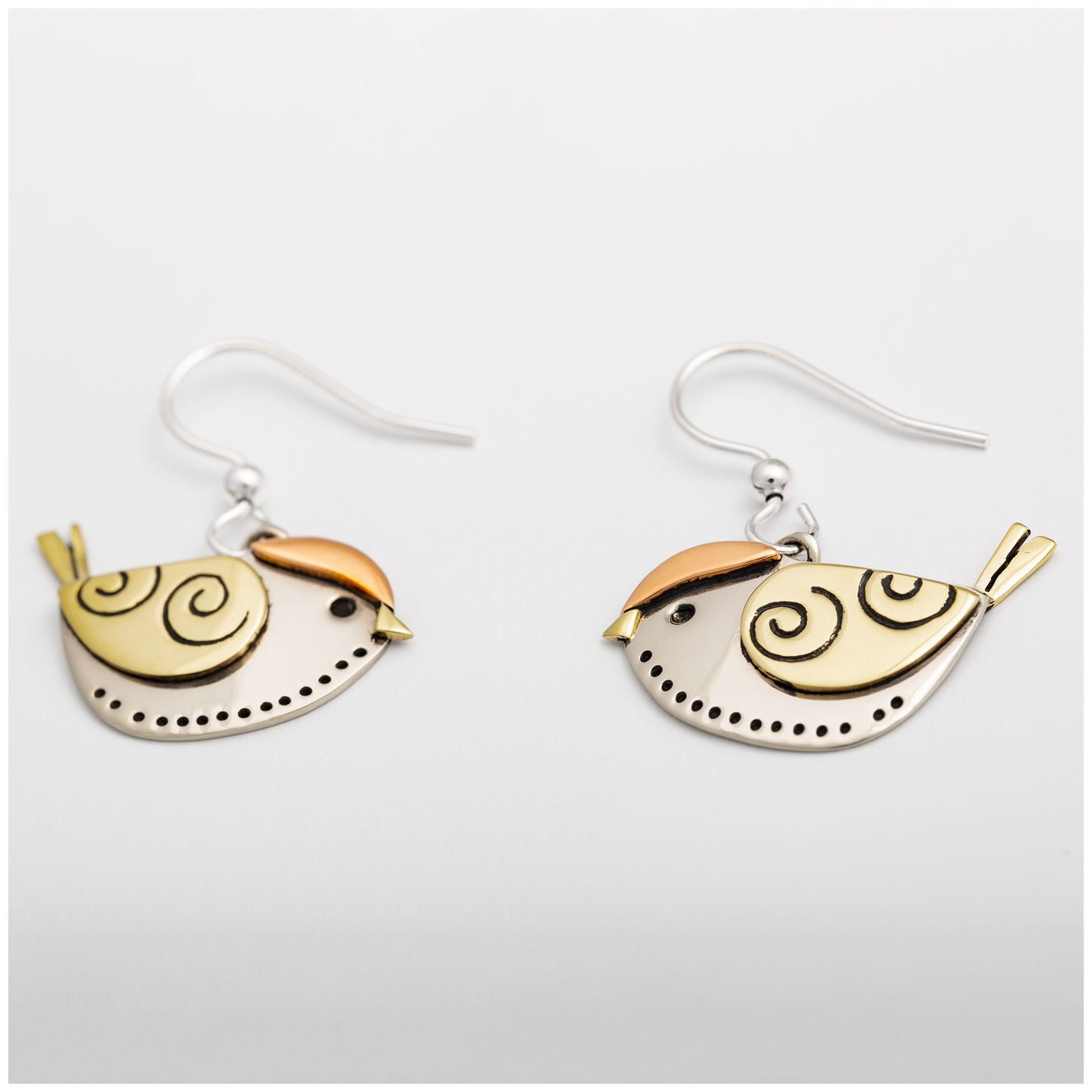 Bird-shaped earrings in silver, copper, and brass on a white background.