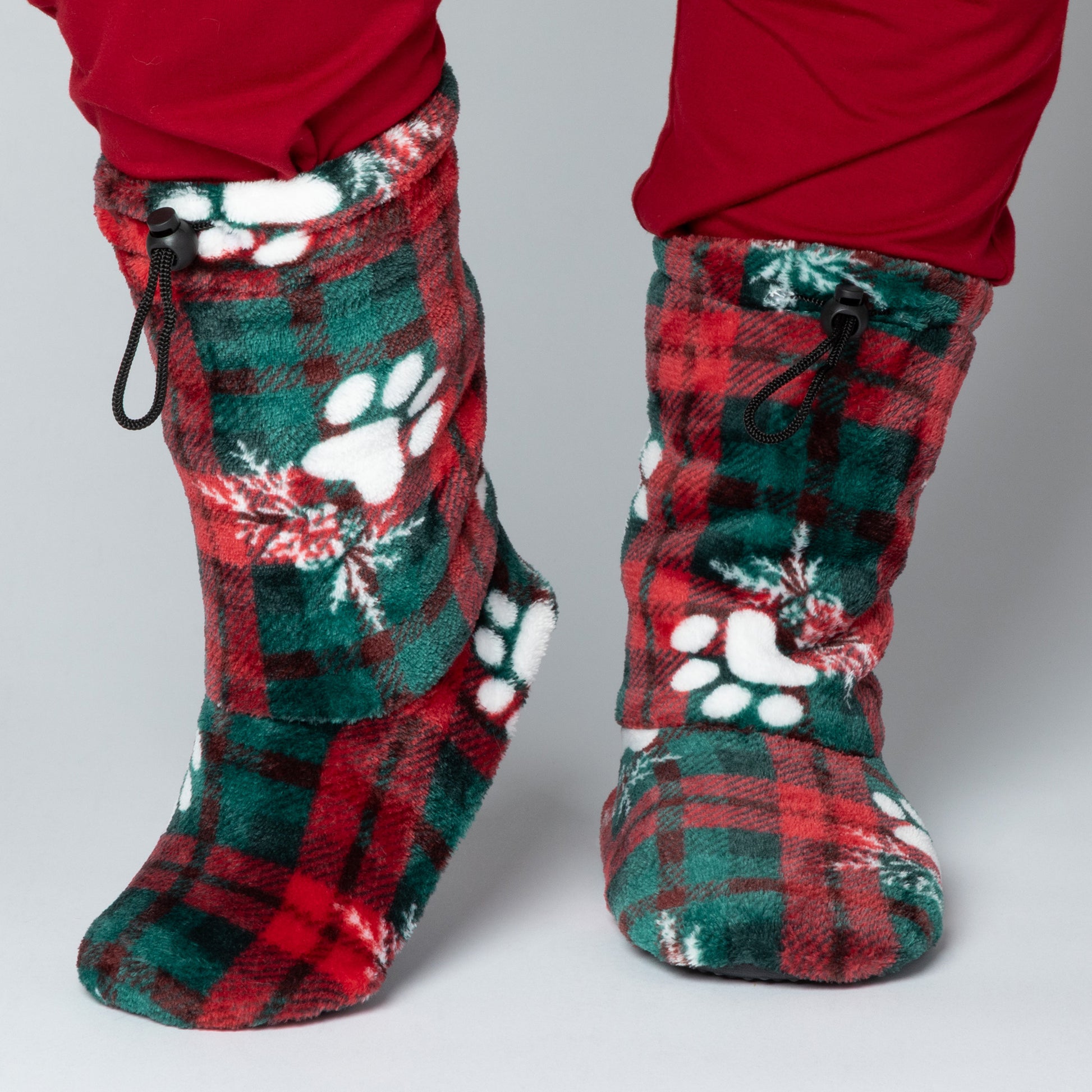 Red and green plaid slipper booties with paw prints and snowflakes, with adjustable toggles on top, against a white background.