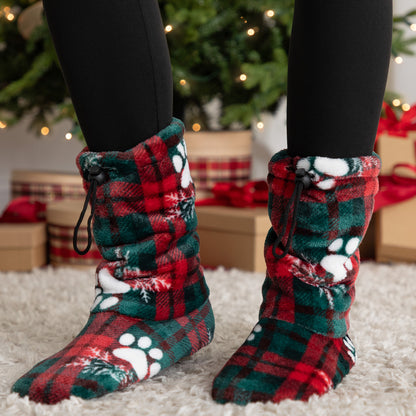 Red and green plaid slipper booties with paw prints worn indoors, Christmas decorations in the background.