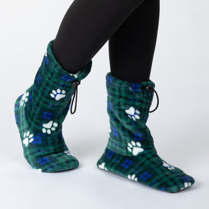 A person wearing plush fleece slipper socks with a green plaid pattern, blue accents, and white paw prints, paired with black leggings, shown against a plain white studio background.