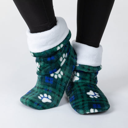 A pair of plush fleece slipper socks with a green and blue plaid pattern, white paw prints, and a white fleece cuff, shown on a person's feet wearing black leggings against a light gray background.