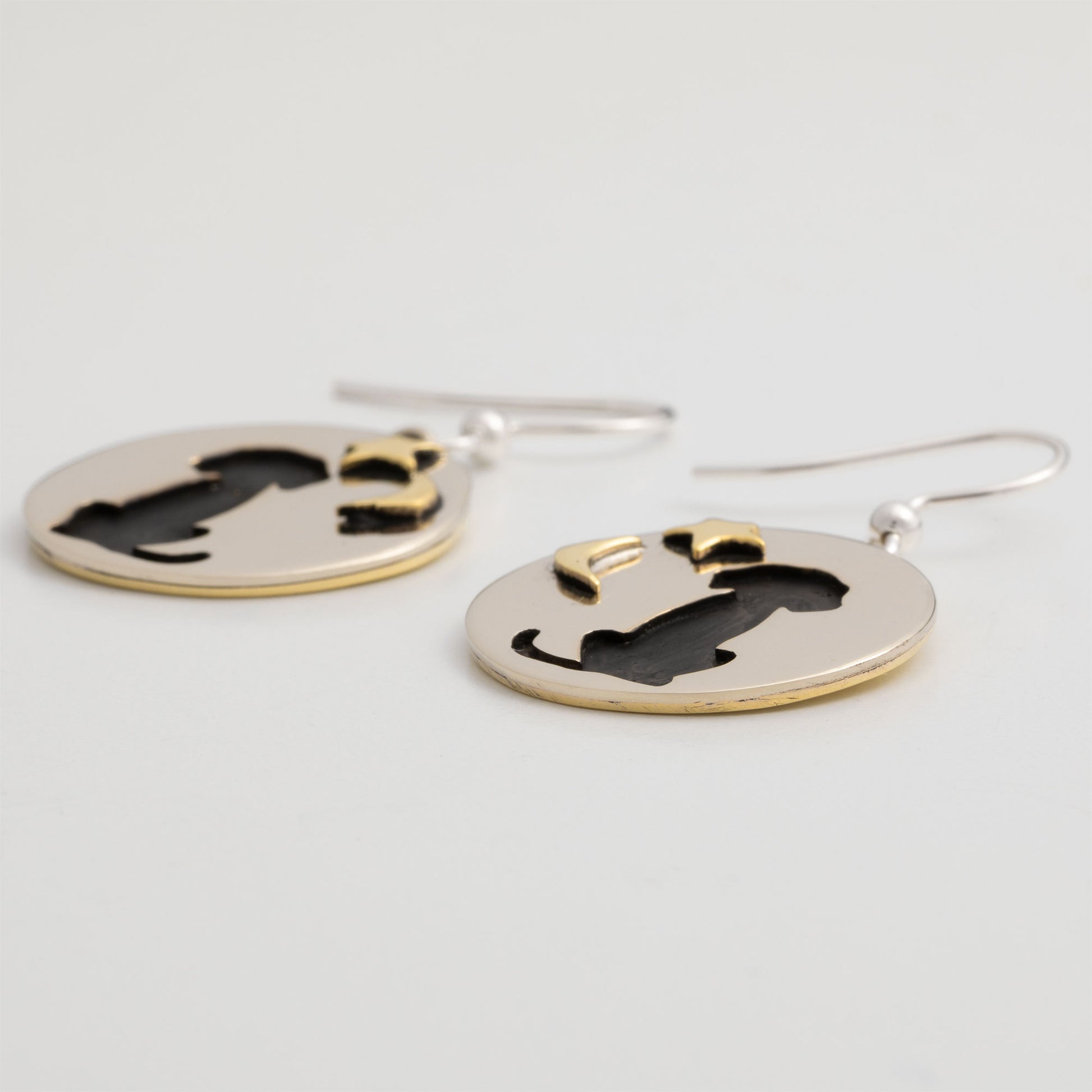 Pair of brass and silver earrings with a dog silhouette, moon and star on a light gray background