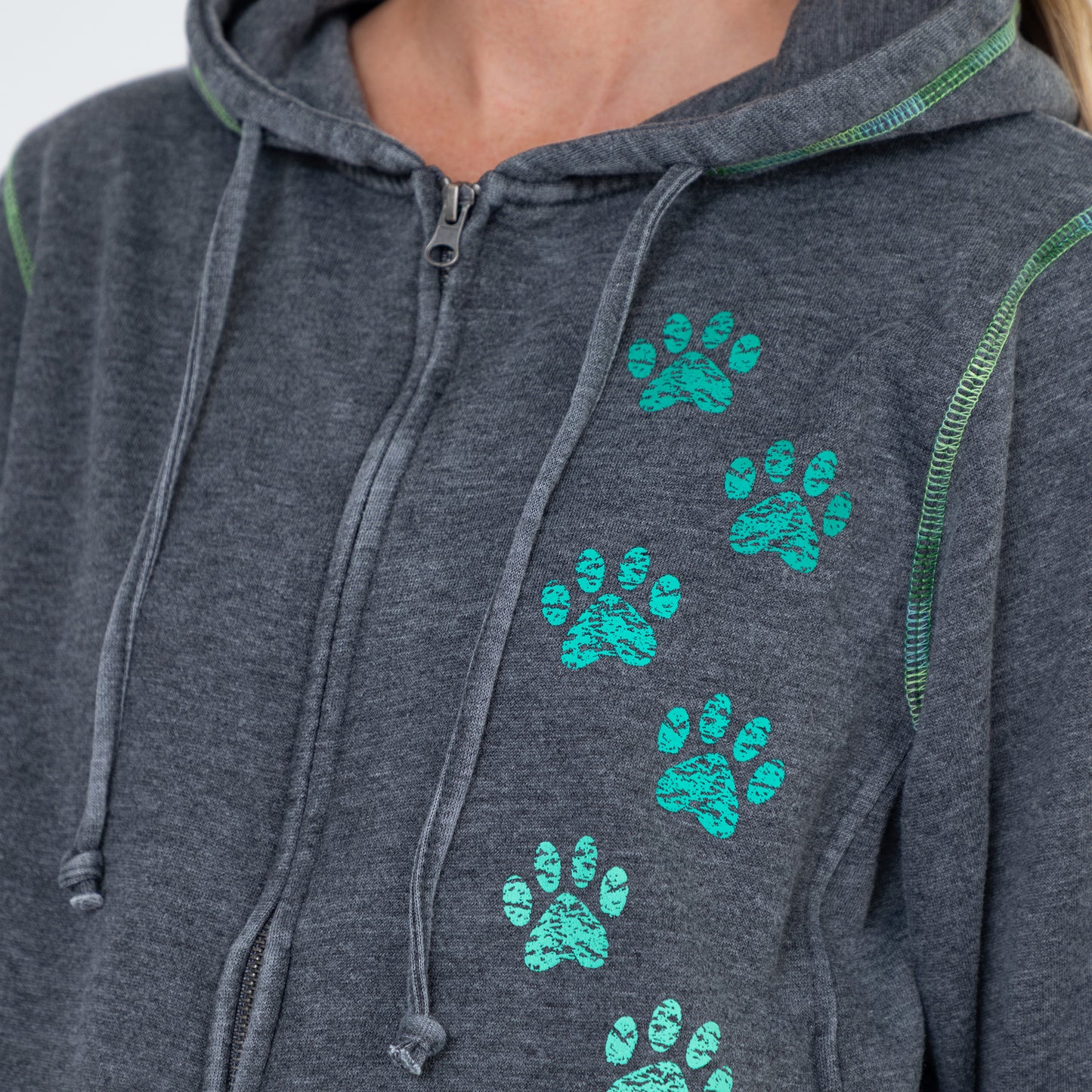 Close-up of a dark heather gray zip-up hoodie worn by a model, featuring a vertical pattern of bright teal paw prints on the front and green contrast stitching.