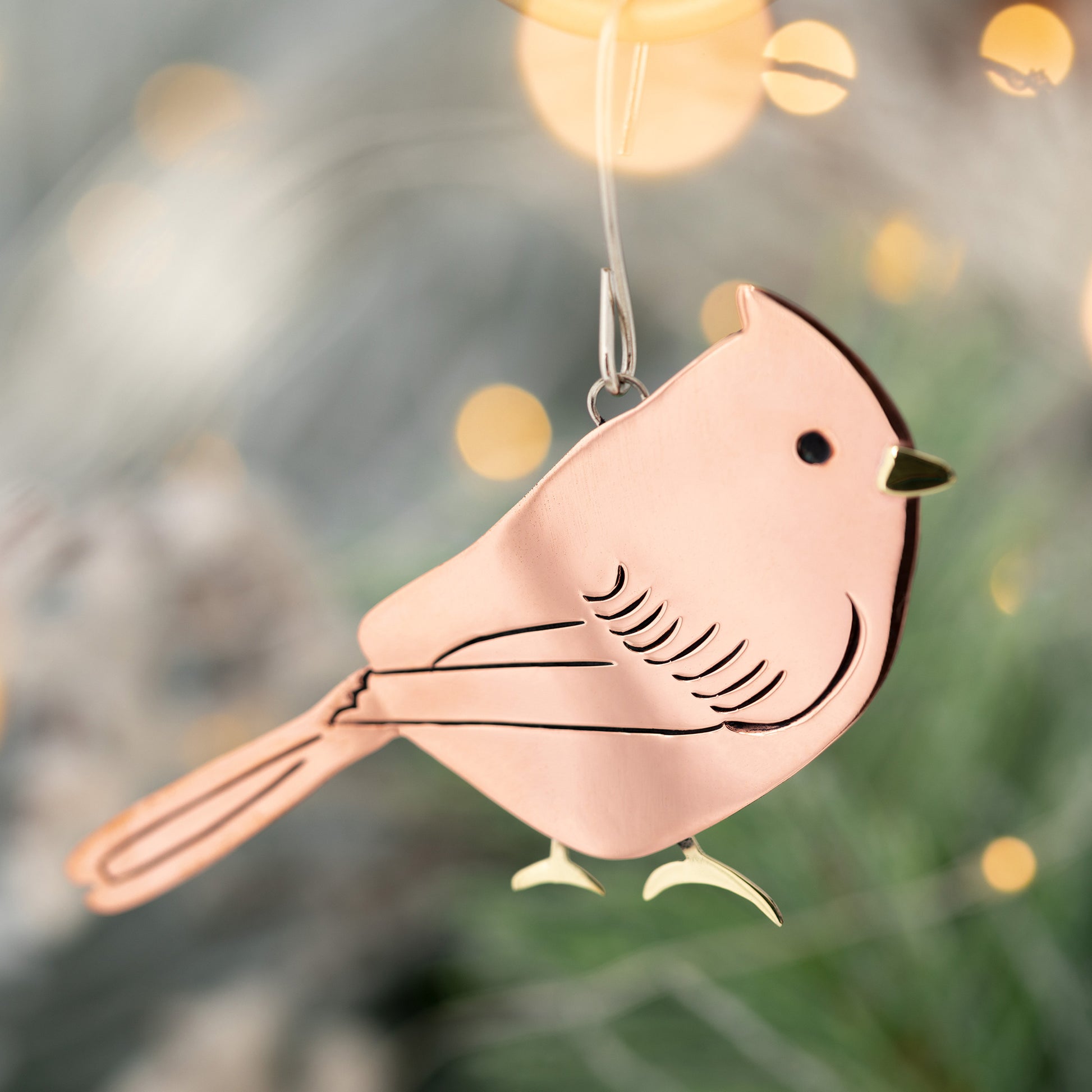 Decorative bird ornament hanging against a blurred Christmas tree background.