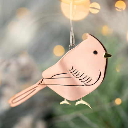 Decorative bird ornament hanging against a blurred Christmas tree background.