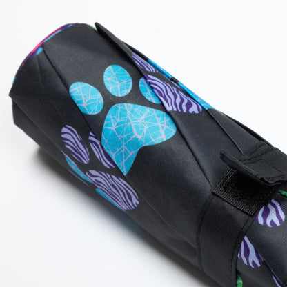 Black umbrella folded up with blue and purple paw print designs on a white background