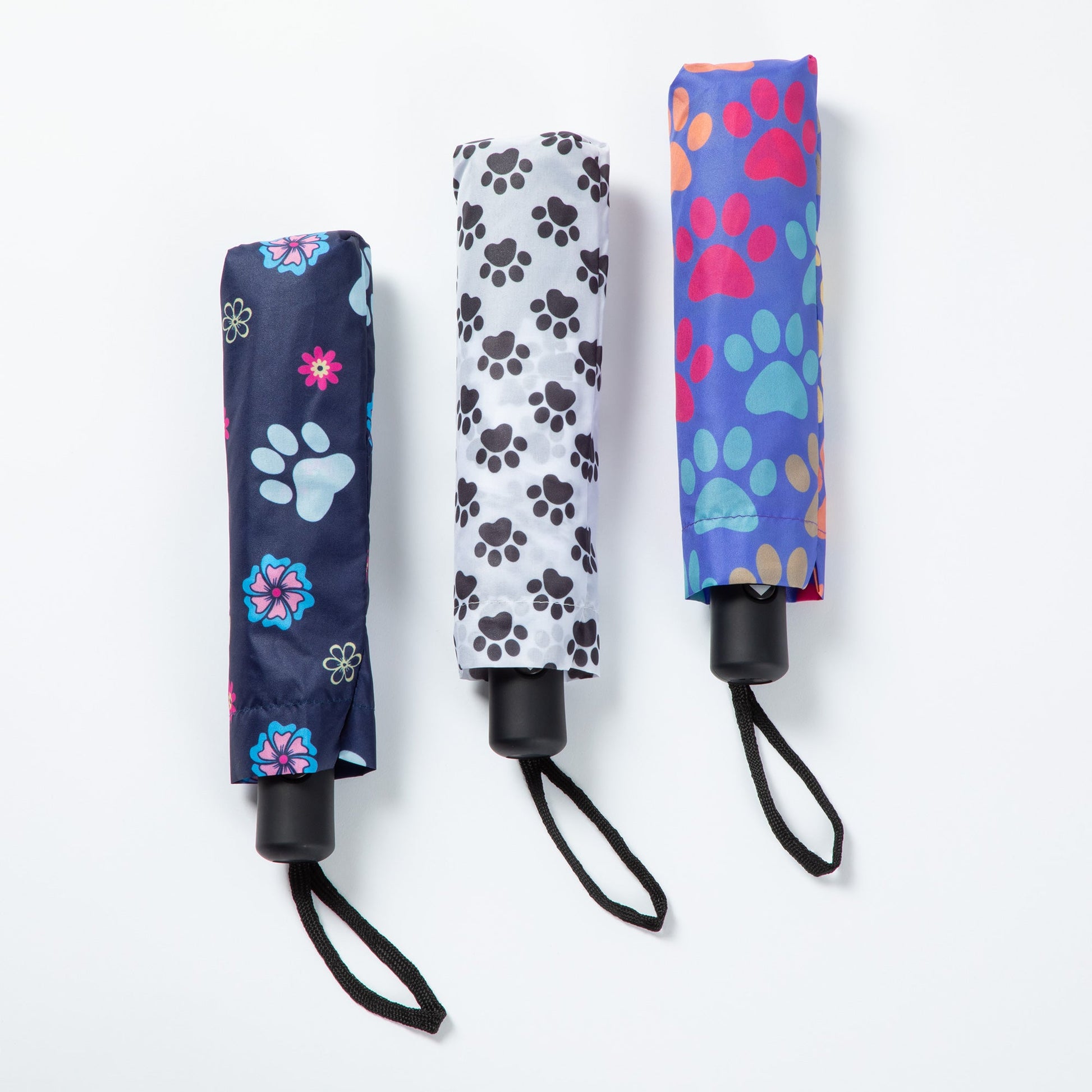 Three paw print patterned umbrellas, folded and with a carrying case over them, against a white background.