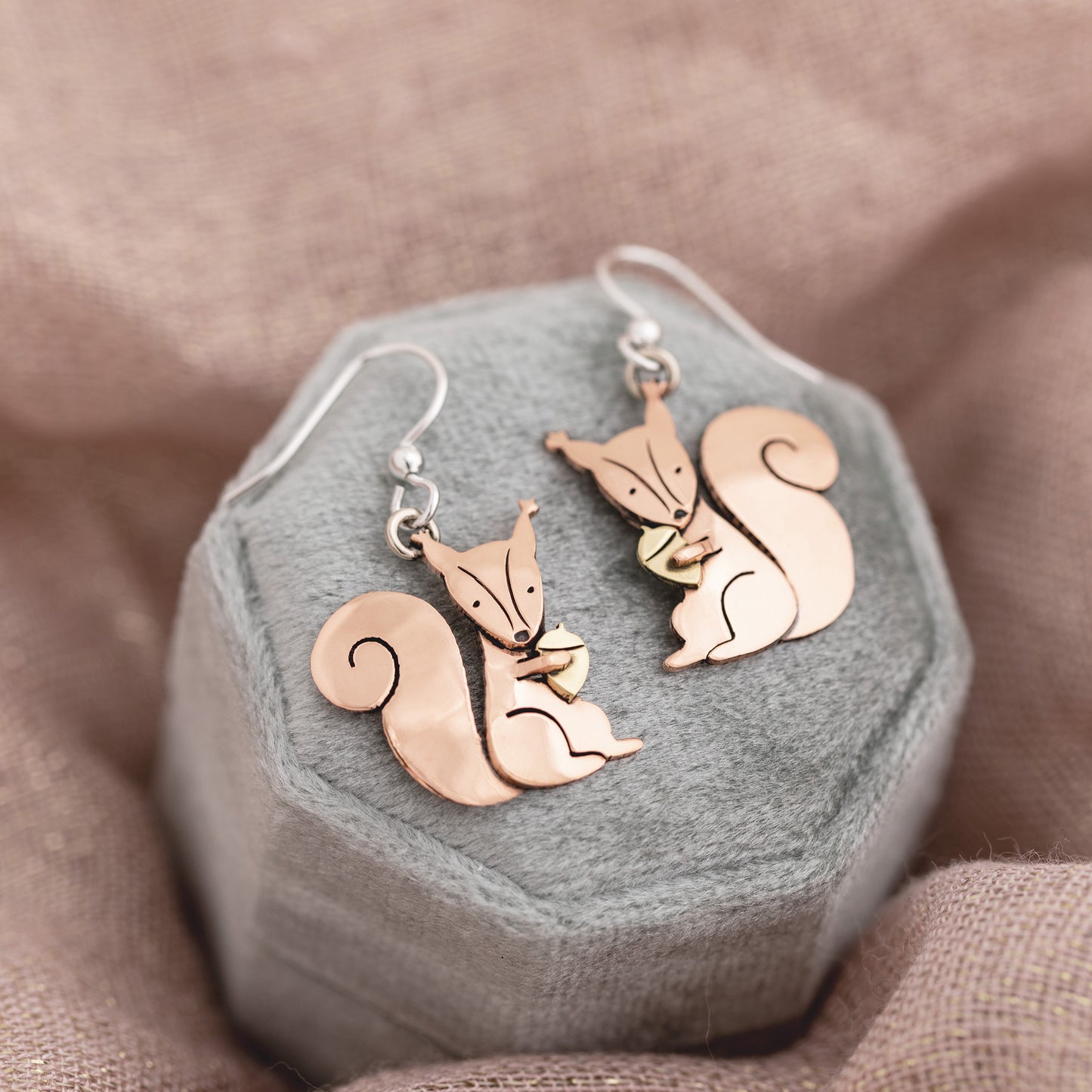 Copper squirrel-shaped earrings on a hexagonal gray jewelry box with a brown fabric background.