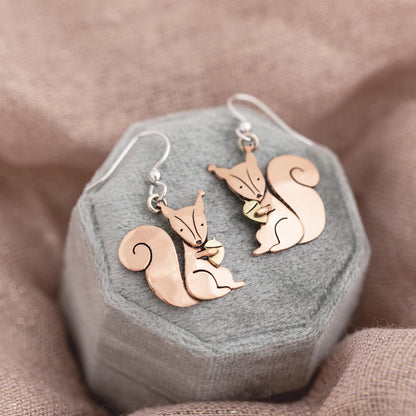 Copper squirrel-shaped earrings on a hexagonal gray jewelry box with a brown fabric background.