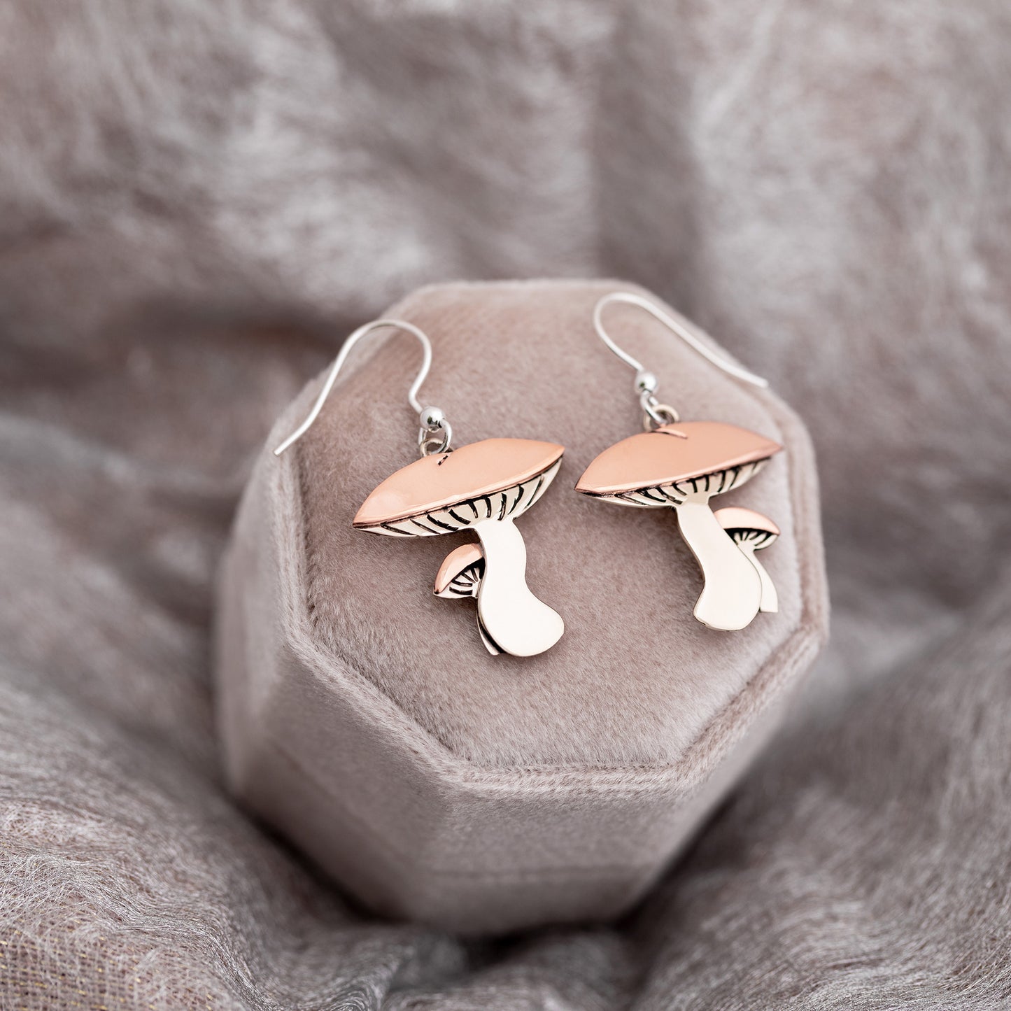 Mushroom-shaped earrings on a gray jewelry box against a neutral fabric background.