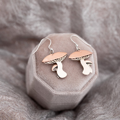 Mushroom-shaped earrings on a gray jewelry box against a neutral fabric background.