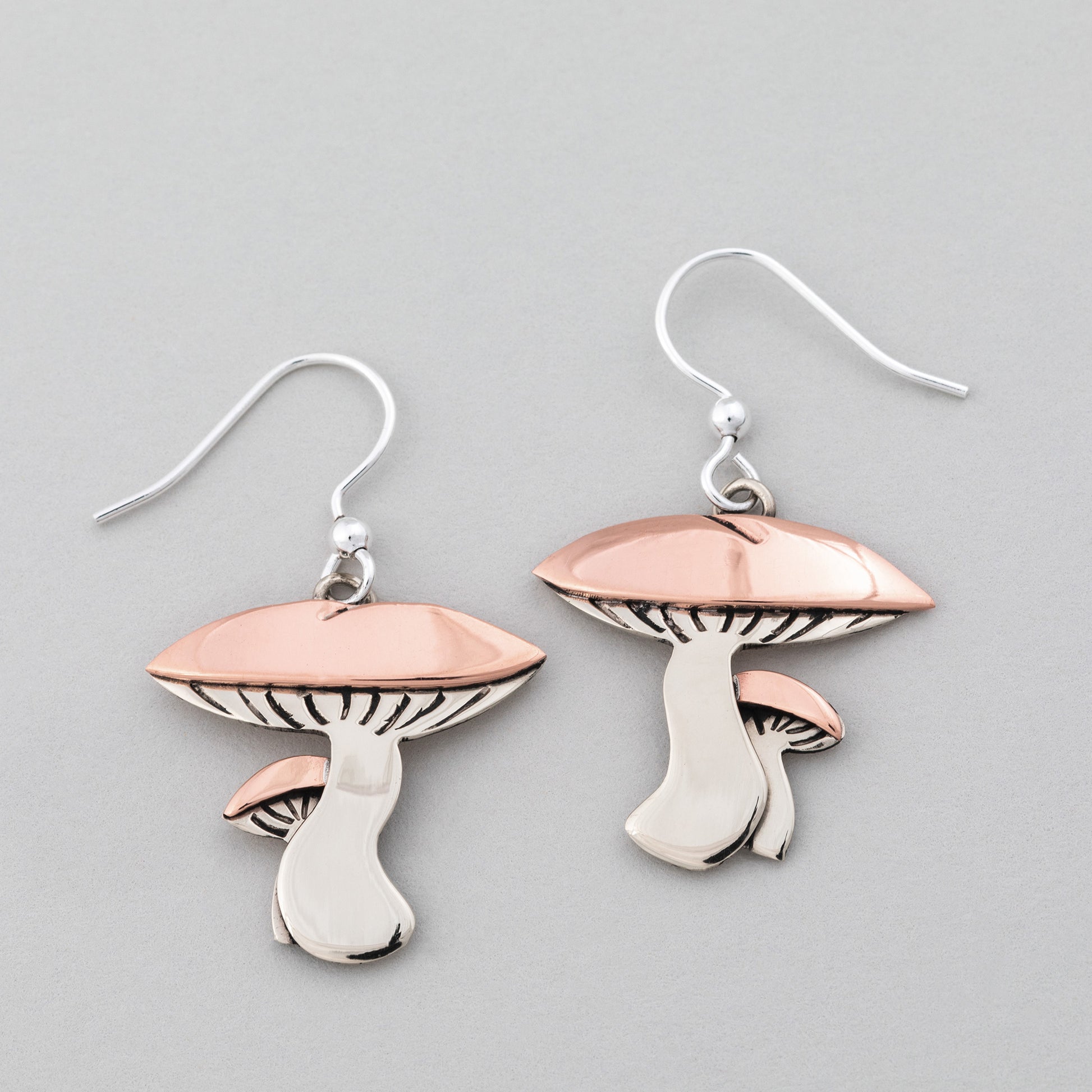Mushroom-shaped earrings with copper and silver on a gray background.