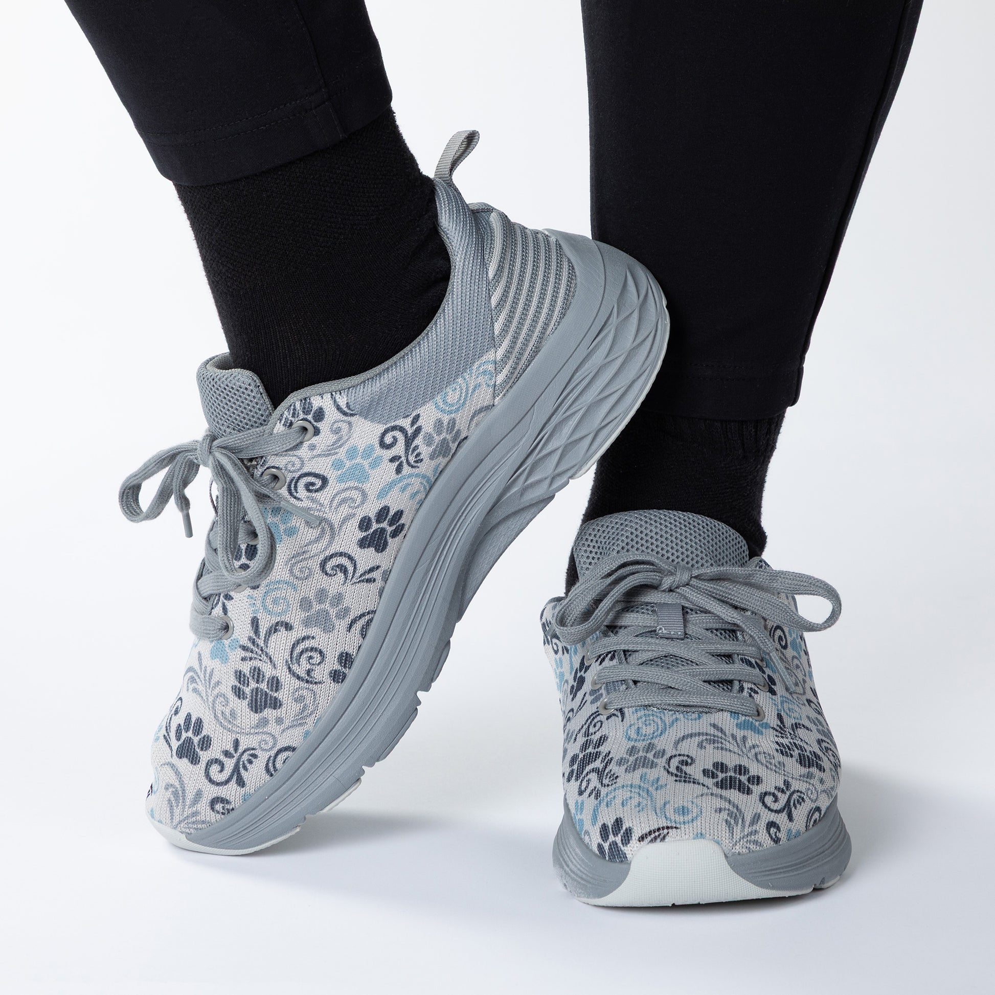 Gray paw print patterned sneakers worn with black leggings on a white background
