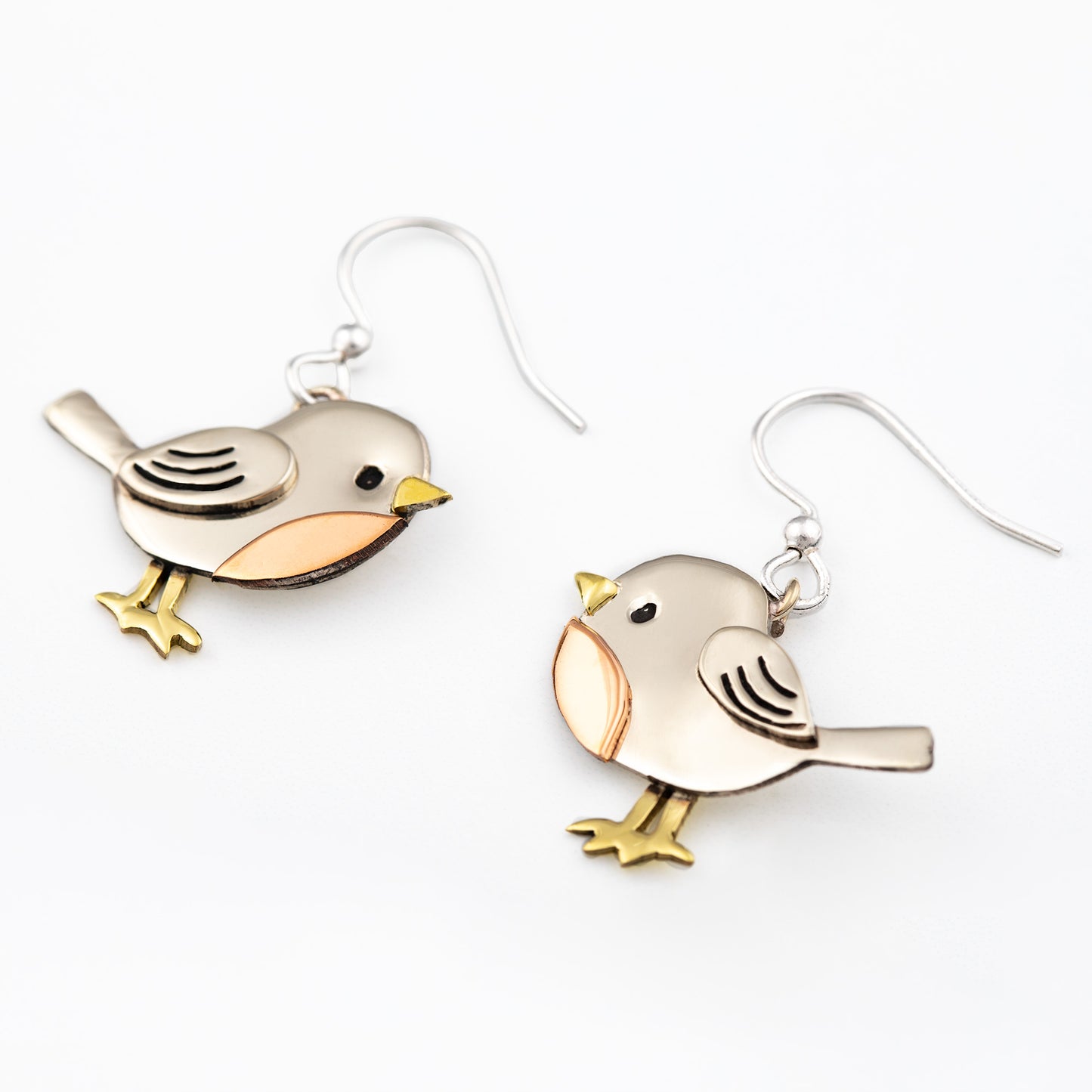 Bird-shaped silver earrings with brass and copper accents on a white background.