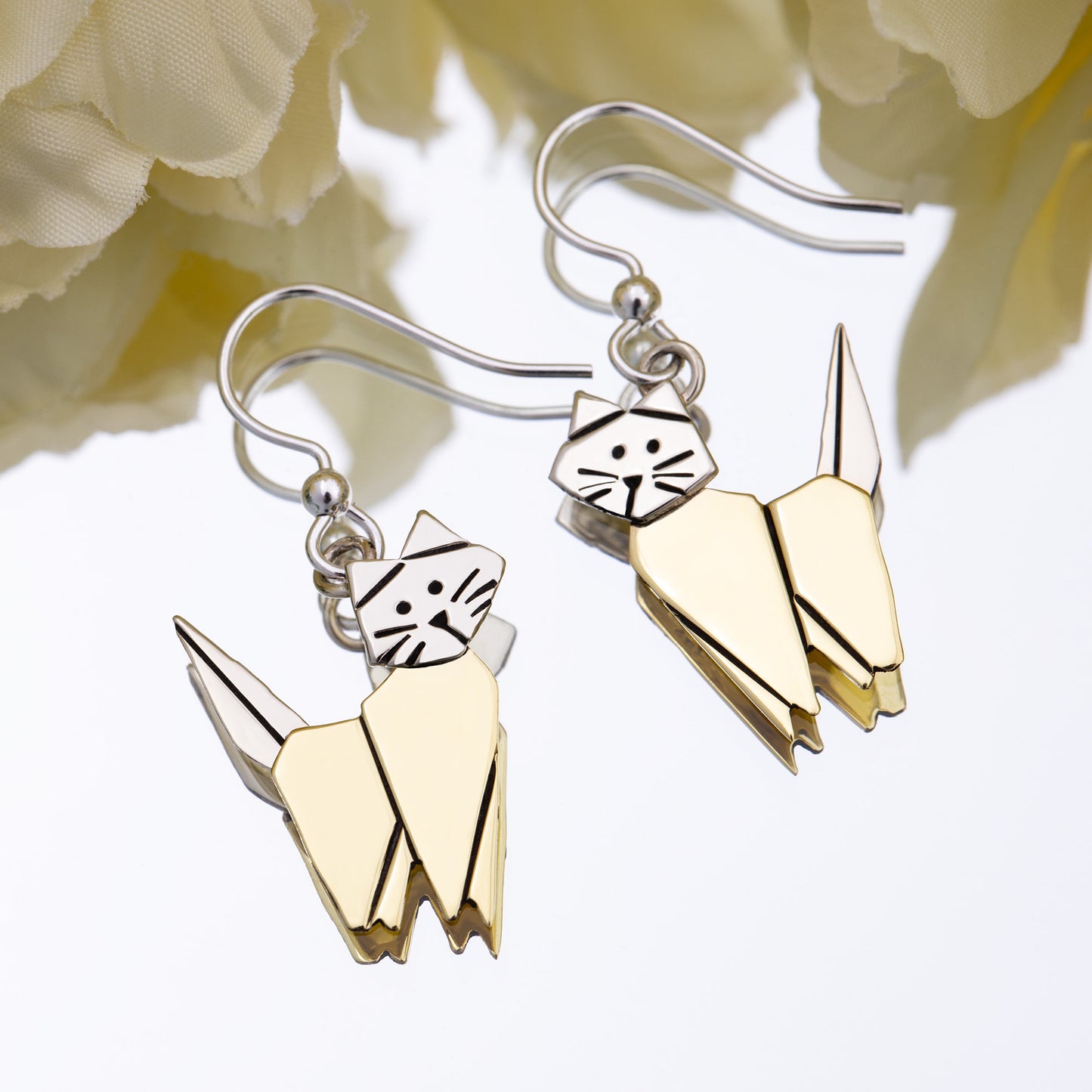 Brass and silver cat-shaped earrings with a white flower background