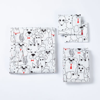 A set of folded sheets, including a larger square piece and three smaller rectangular pieces, all printed with a playful black-and-white dog pattern and small red bow tie and tie accents, arranged on a clean white background.