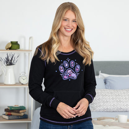 Woman wearing a black thermal long sleeve shirt with a colorful paw design in a bedroom setting.