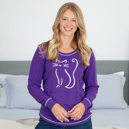 A woman smiling and wearing a long sleeve thermal top in purple with a sketched silhouette of a cat design in white.