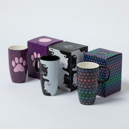 Three ceramic mugs with paw-themed designs are displayed alongside their packaging boxes on a light gray background. The mugs feature a purple paw print, a black-and-white cat silhouette, and a multicolor pattern of tiny cat paws.