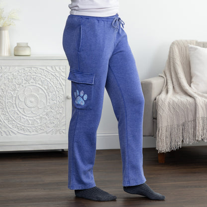 A person wearing heathered blue lounge pants with a drawstring waist and a cargo pocket featuring a blue paw print, standing in a living room setting.