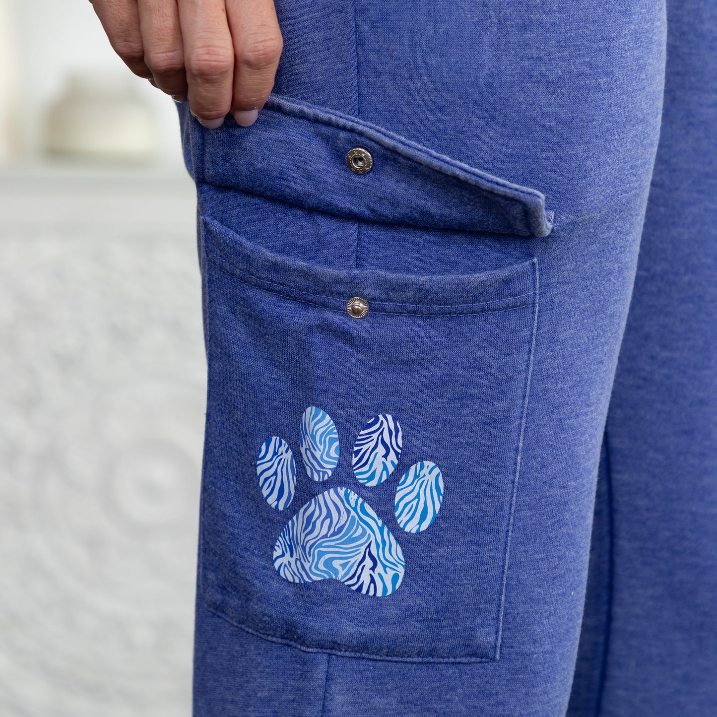 Close-up of a person wearing heathered blue jogger pants with a cargo pocket featuring a blue and white zebra-patterned paw print graphic.