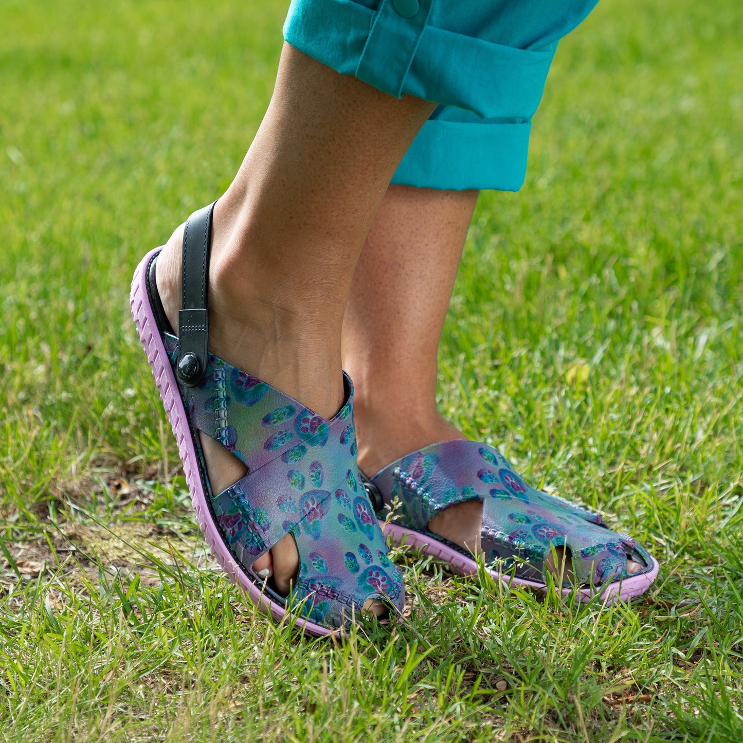 A person wearing colorful butterfly-print slingback sandals with a black strap, standing on green grass.