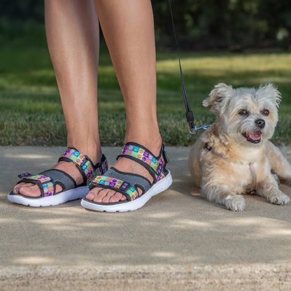 A person next to a small dog wearing colorful leash. Model wearing colorful sandals