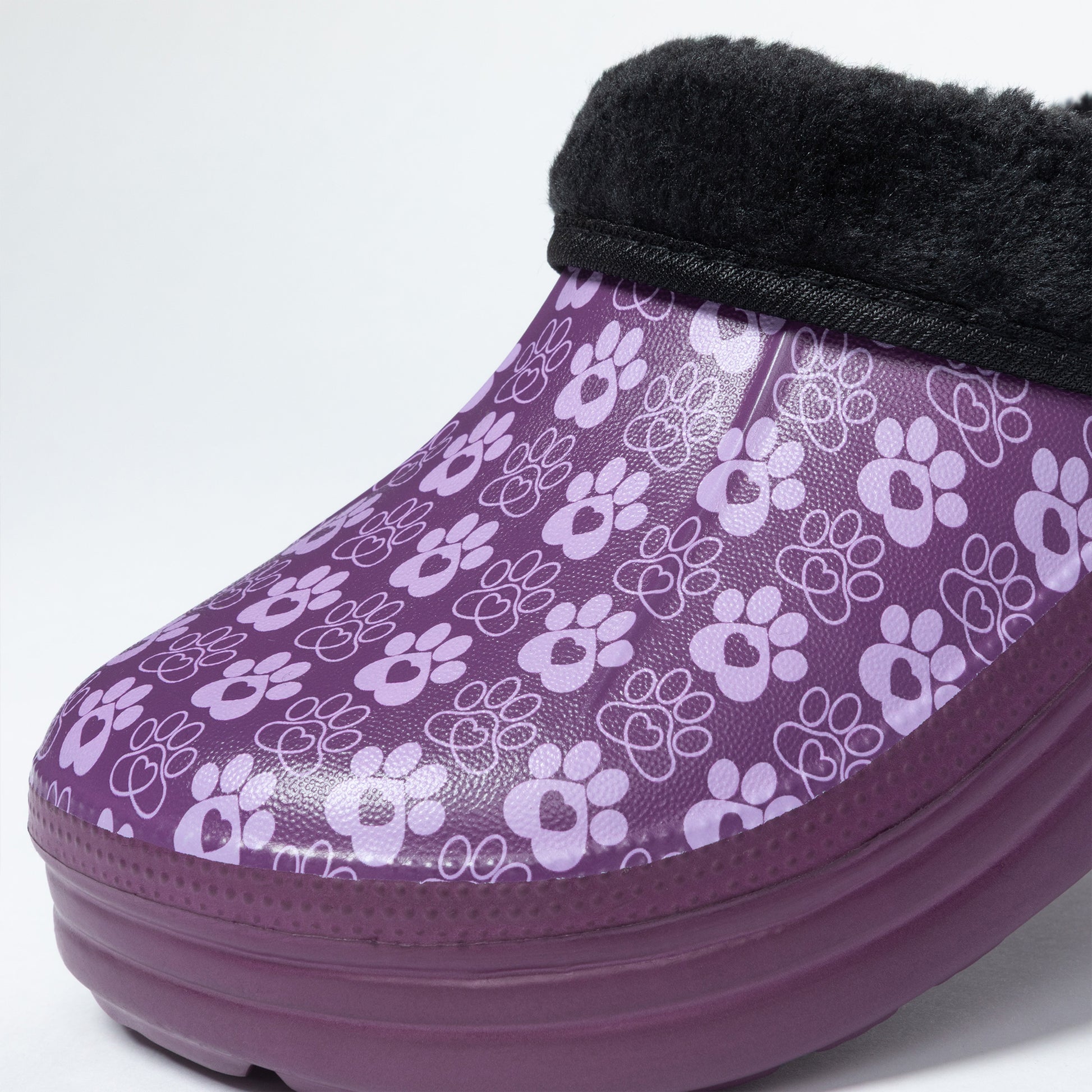 A purple slip-on clog featuring a repeating white paw print pattern, a thick purple sole, and a black faux-fur trim at the top, shown against a plain white background.