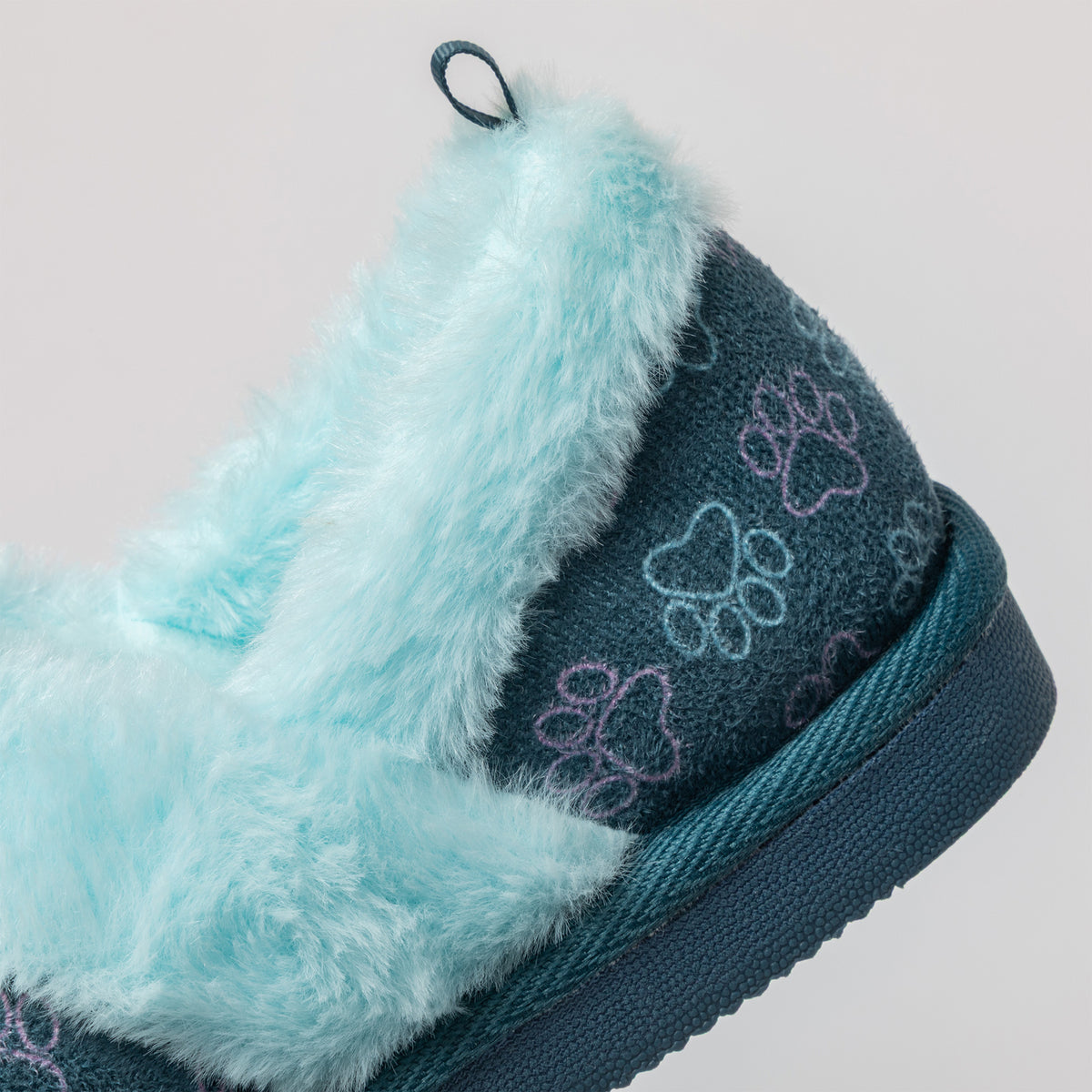 Close-up of a plush pet slipper with a light blue faux fur trim and a dark teal fabric body featuring embroidered paw prints in light blue and lavender.
