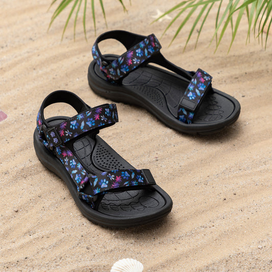 Stylish floral-patterned sandals resting on sandy beach, surrounded by seashells.