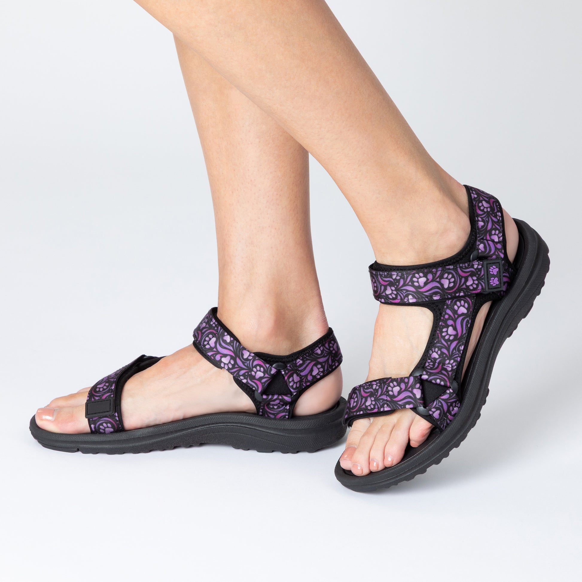 Purple paw print patterned sandals worn by a person on a white background