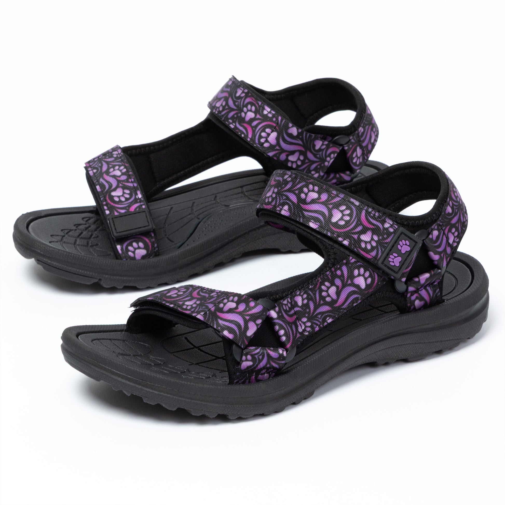 Pair of black sandals with purple paw print straps on a white background