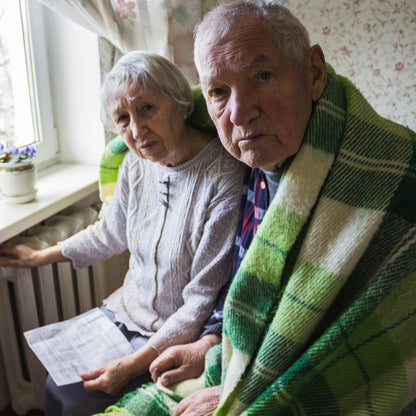 Two elderly people sitting together, one holding a piece of paper, in a home setting.