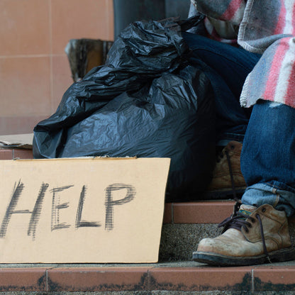 Person sitting on steps with a 'HELP' sign, surrounded by belongings