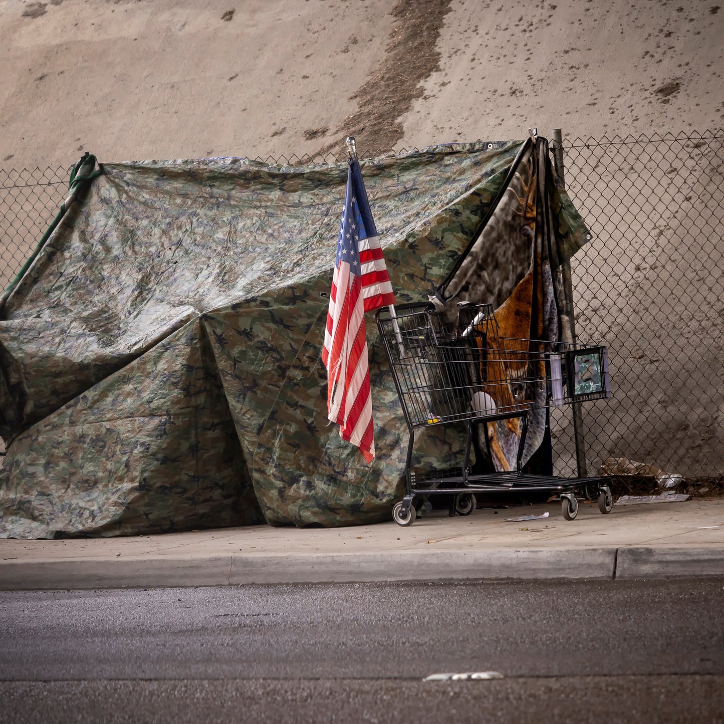 Camouflage tent with American flag and shopping cart on a street corner